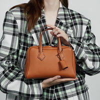 Woman in plaid blazer holding a brown leather handbag with top handles