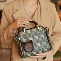 Person holding a patterned handbag with a cat face charm