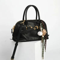 Black leather handbag with gold hardware and baseball-themed keychain, white background