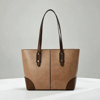 Brown leather tote bag with dark handles on white table, minimalist background