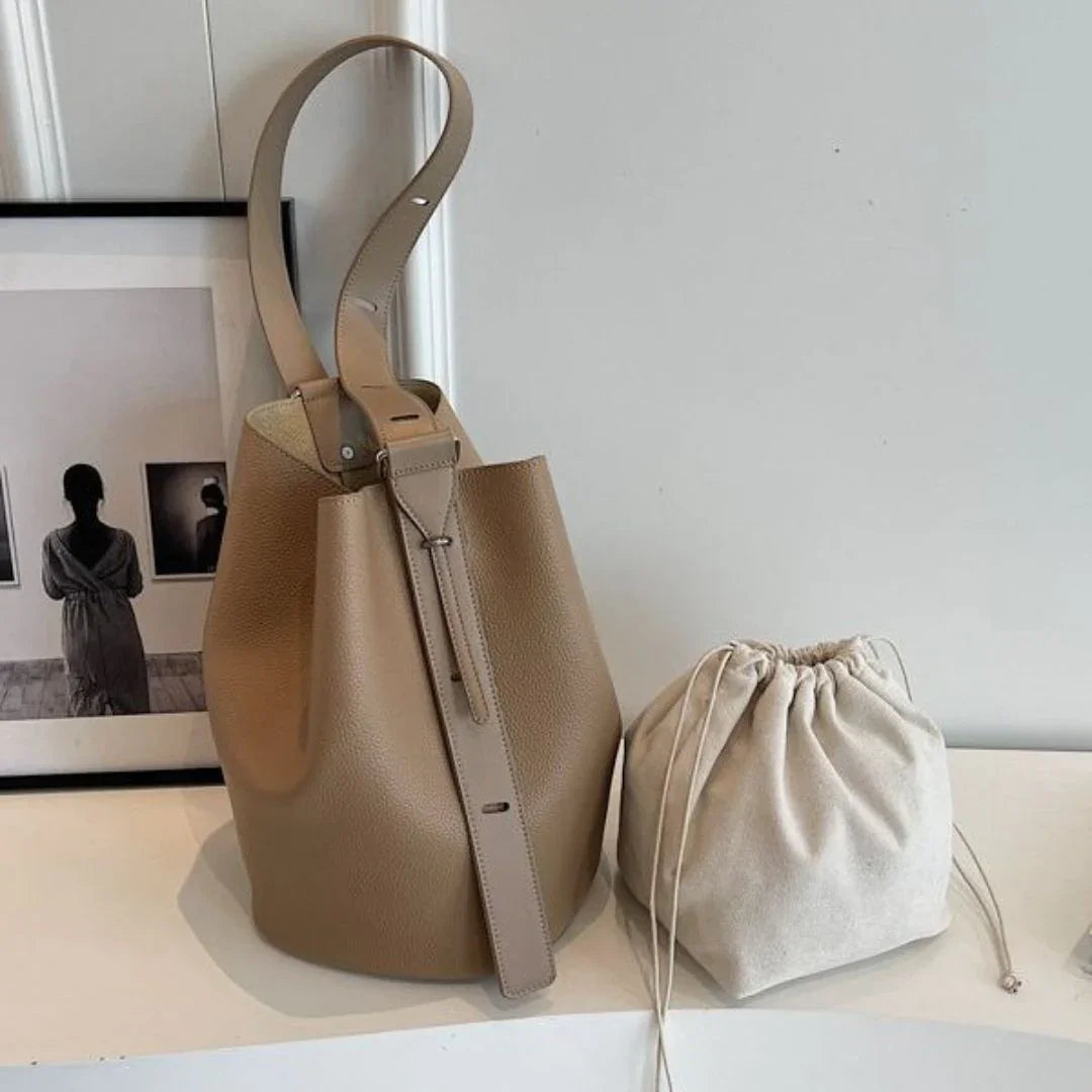 Beige leather bucket bag and cream drawstring pouch on white shelf, minimal decor