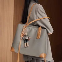 Woman with large gray tote bag featuring tan leather accents and bunny keychain