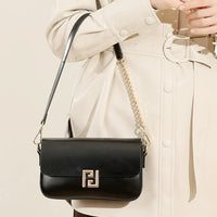 Black leather crossbody bag with gold chain on beige belted trench coat