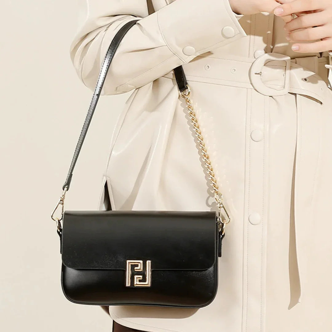 Black leather crossbody bag with gold chain on beige belted trench coat
