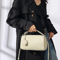Woman in black trench coat holding a textured cream leather handbag