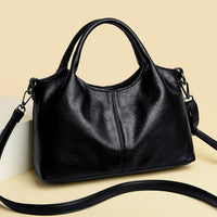 Black leather handbag with handles and shoulder strap on beige background