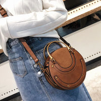 Woman wearing a stylish brown round leather crossbody bag with gold handles and denim skirt