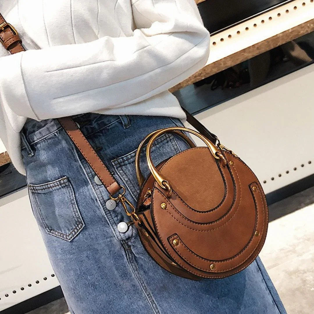 Woman wearing a stylish brown round leather crossbody bag with gold handles and denim skirt