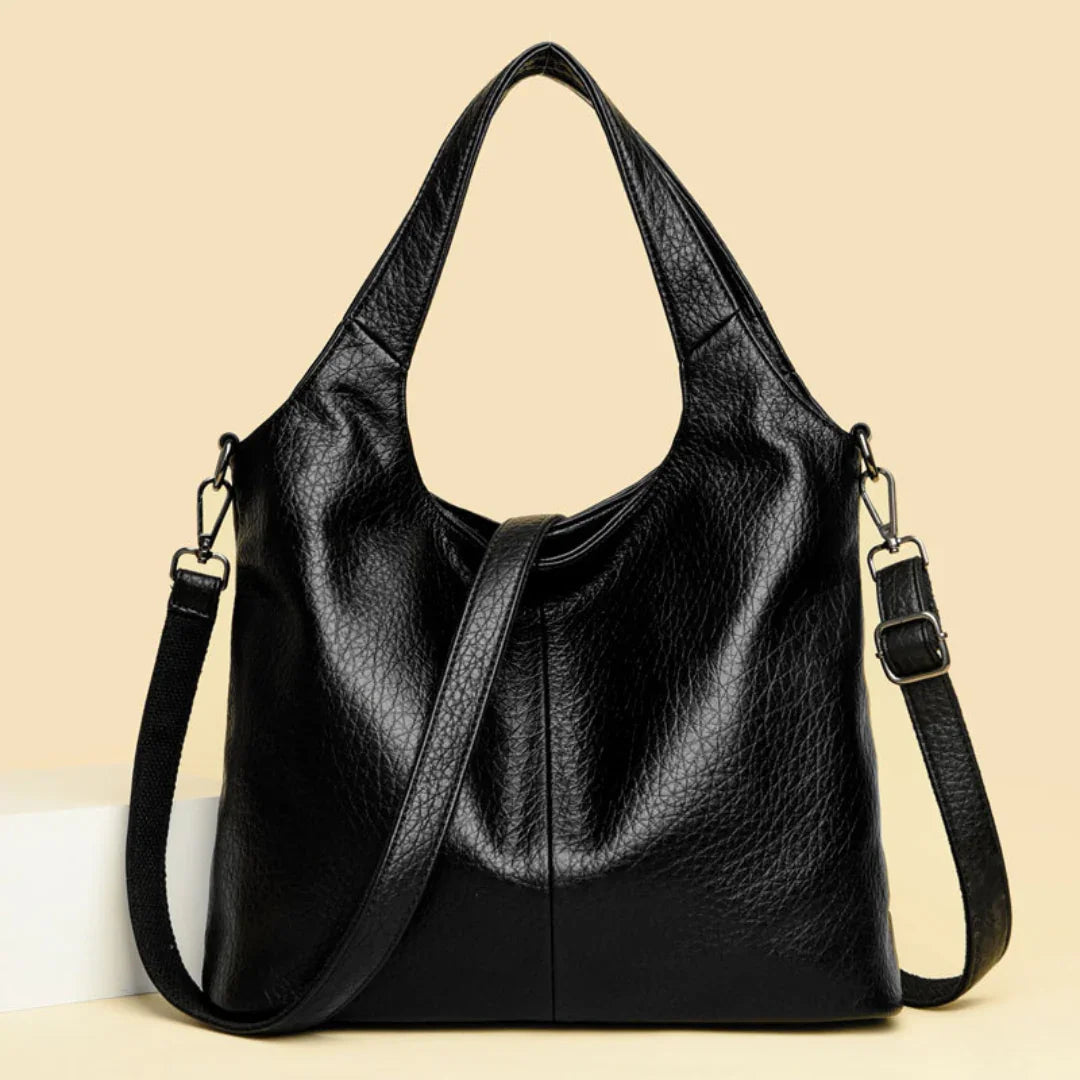 Black leather tote handbag with textured finish and adjustable shoulder strap on beige background.