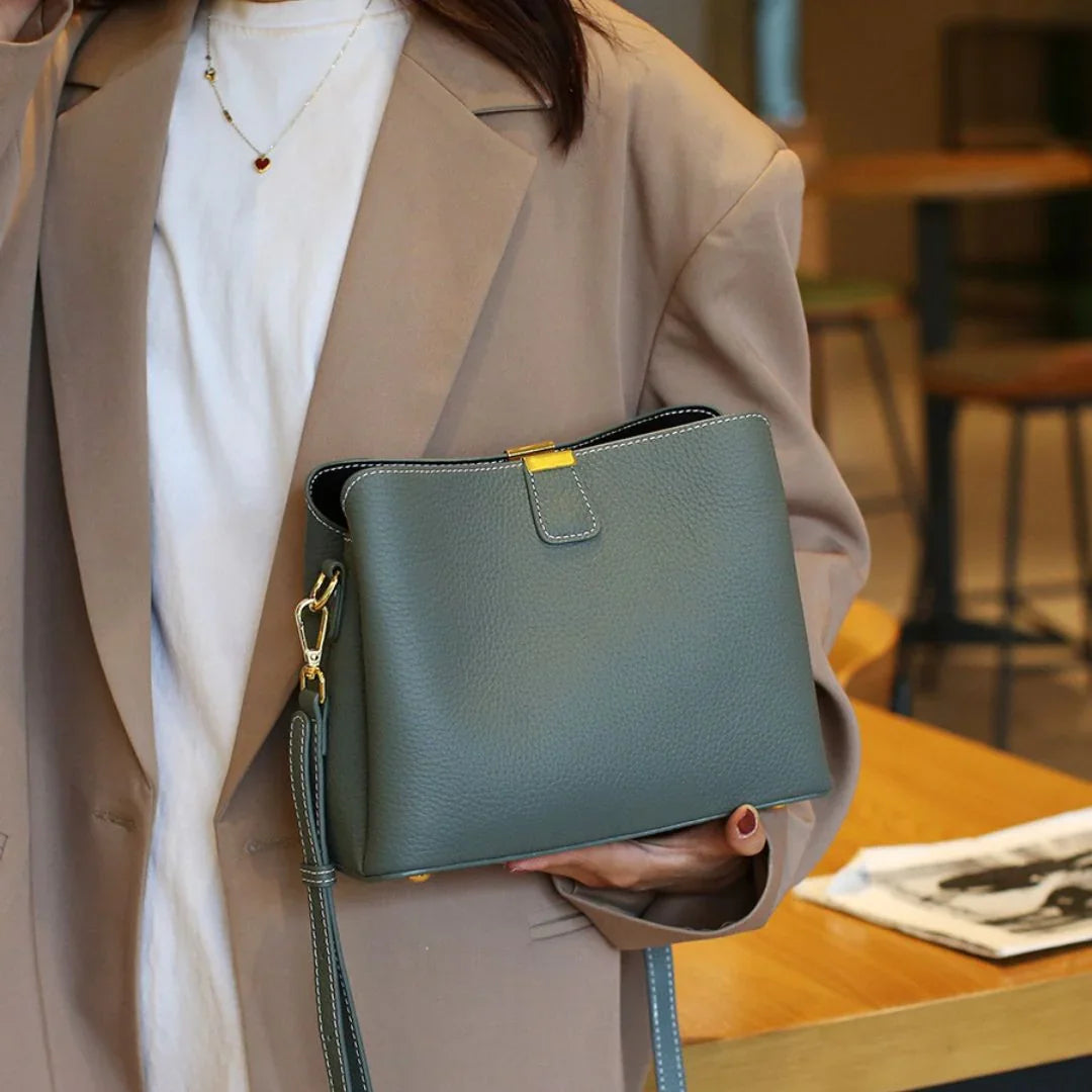 Woman in beige blazer holding green leather crossbody bag with gold accents in cafe