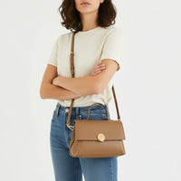 Woman wearing beige t-shirt, blue jeans, and carrying a tan leather crossbody handbag