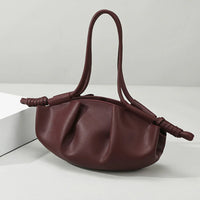 Burgundy leather ruched handbag with knotted handles on a white table