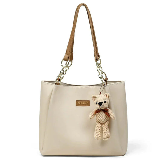 Beige leather tote bag with brown handles, gold chain, and teddy bear keychain charm