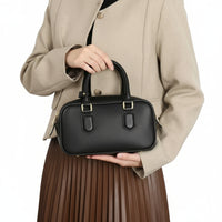Woman in beige blazer holding black leather handbag with gold hardware