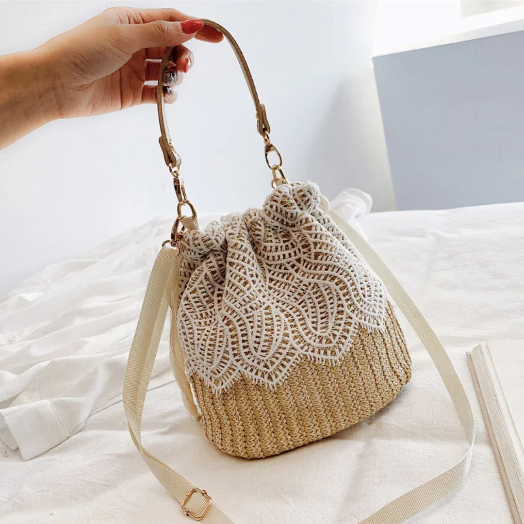 Hand holding a beige crochet lace bucket bag with woven texture and fabric strap on a bed