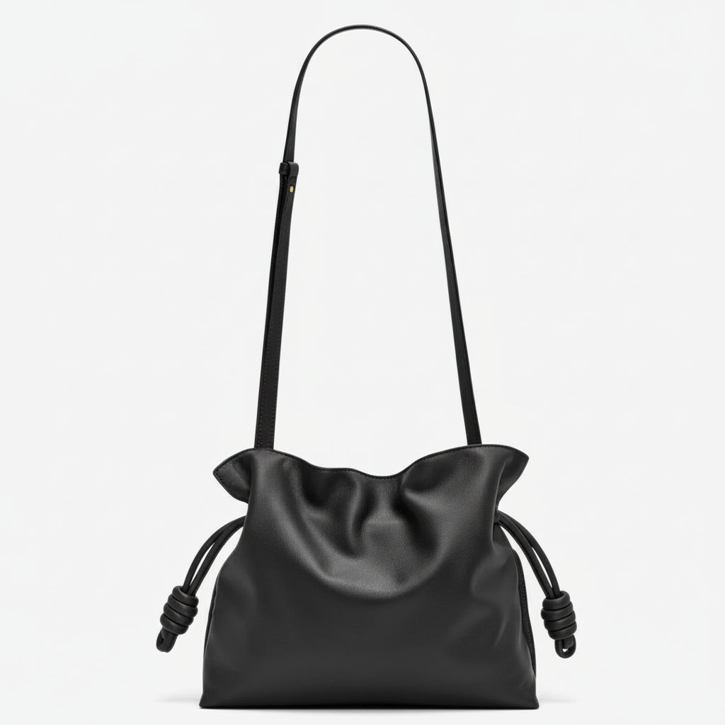 Black leather crossbody bag with drawstring sides and adjustable strap on white background