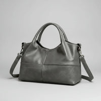 Gray leather handbag with short handles and detachable shoulder strap on plain background