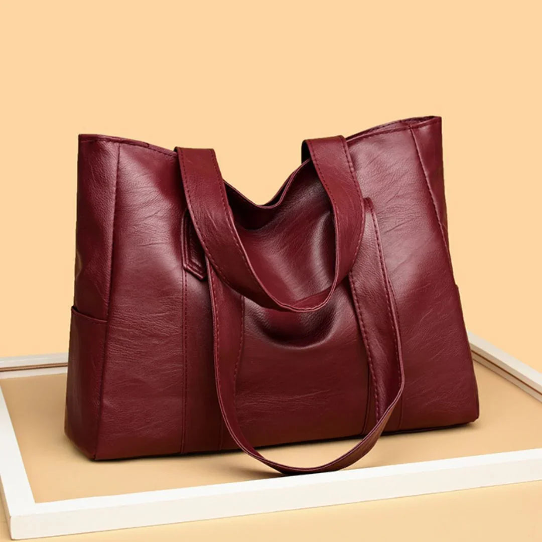 Large maroon leather tote bag with double handles on beige background