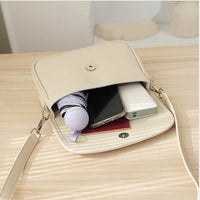 Beige crossbody bag with umbrella, smartphone, and power bank on light wood table