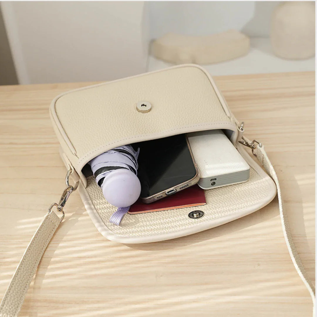 Beige crossbody bag with umbrella, smartphone, and power bank on light wood table