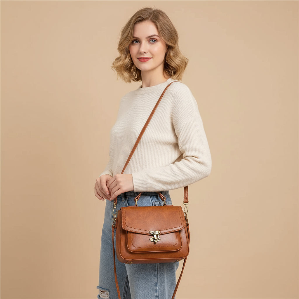Woman in white sweater and jeans modeling a brown leather crossbody bag with gold clasp