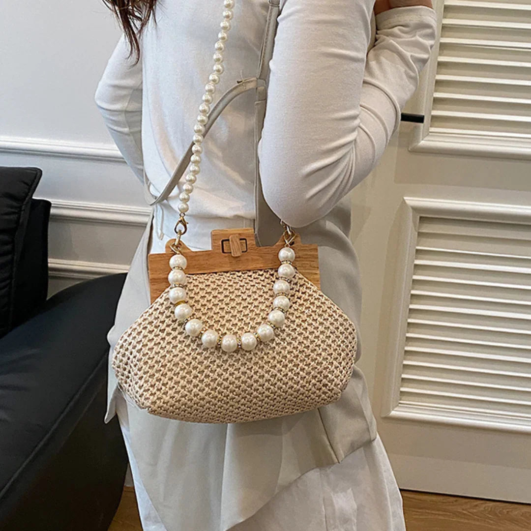 Woman holding woven straw handbag with wooden frame and pearl beaded handle, indoor setting