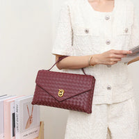 Woman in textured white outfit holding woven burgundy clutch handbag with gold clasp