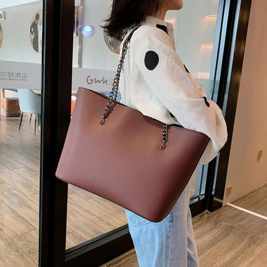Woman in polka dot shirt with large brown tote bag and chain strap indoors