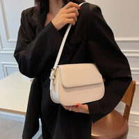 Woman in black blazer holding a white leather shoulder bag indoors