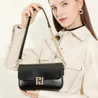 Woman in cream jacket holding black leather shoulder bag with gold chain strap