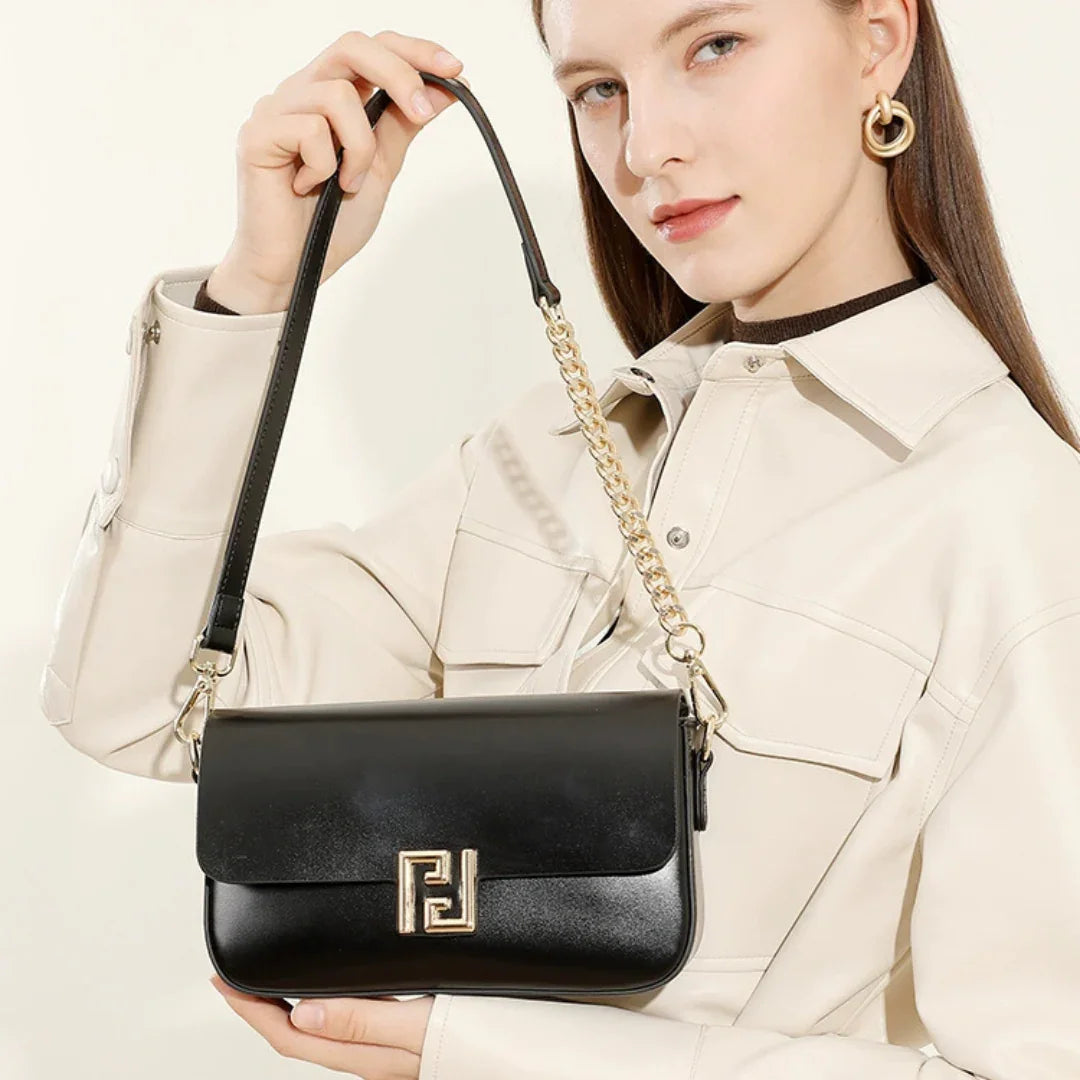 Woman in cream jacket holding black leather shoulder bag with gold chain strap