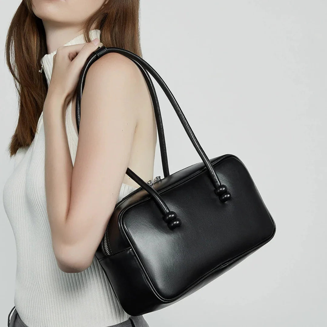 Woman with black leather shoulder bag and sleeveless white top against neutral background