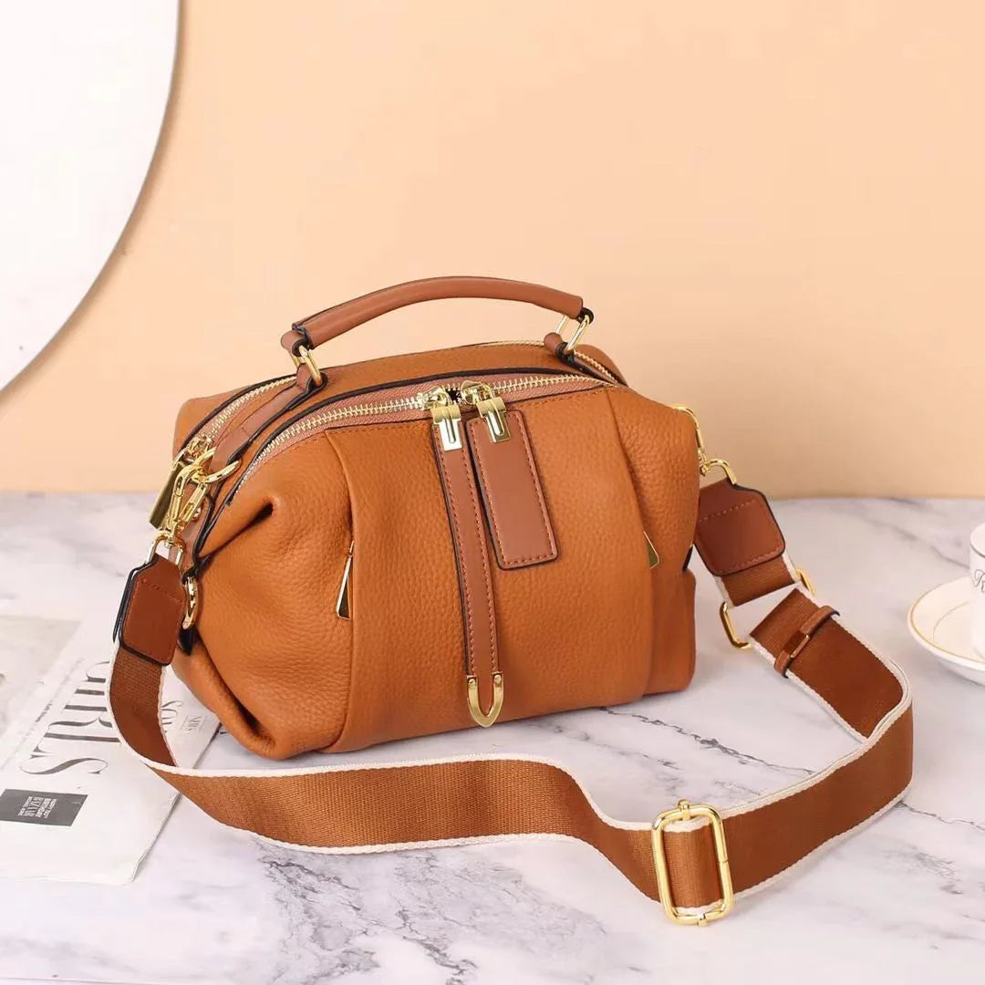 Brown leather crossbody handbag with gold zipper on marble table