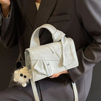 Woman in black blazer holding light grey denim handbag with furry keychain