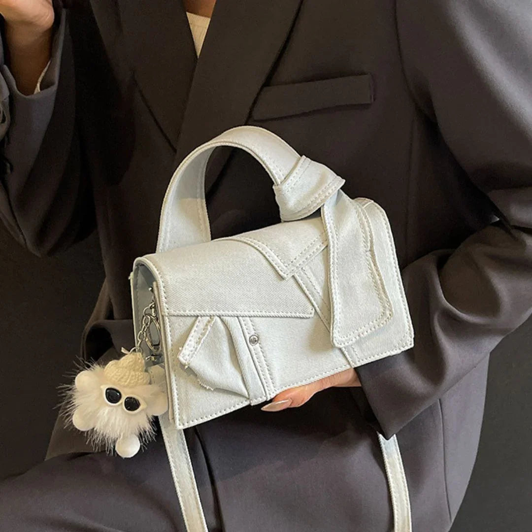 Woman in black blazer holding light grey denim handbag with furry keychain