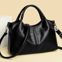 Black leather handbag with shoulder strap on beige background
