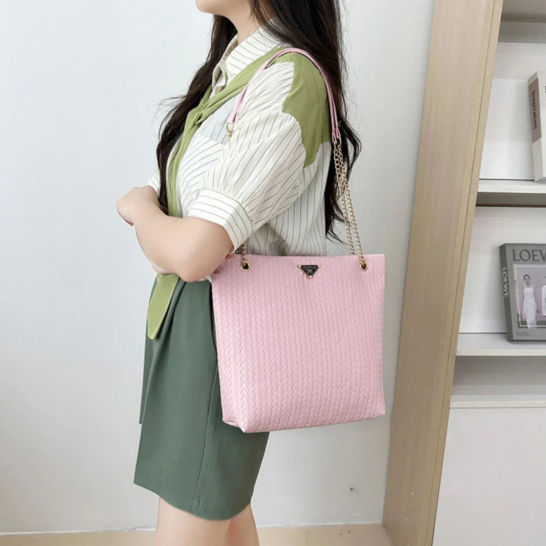 Woman carrying pink textured tote bag with gold chain straps indoors