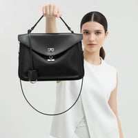 Woman in white top holding black leather handbag with silver hardware against a light background