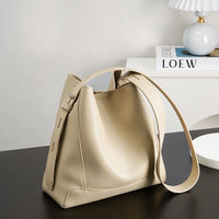Beige leather bucket bag with adjustable strap on black table, modern decor in background