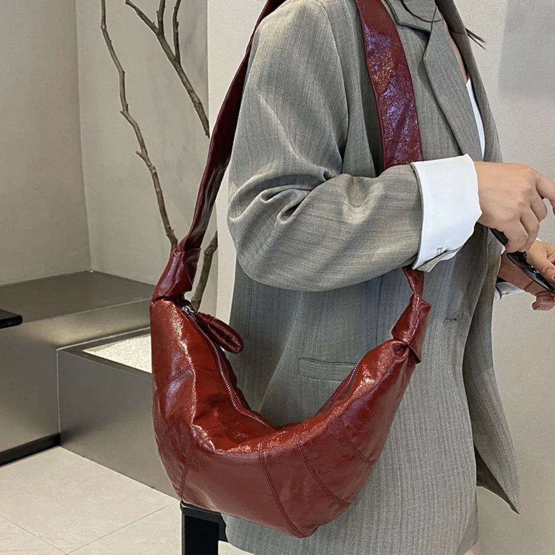 Woman in a grey blazer holding a red leather shoulder bag indoors