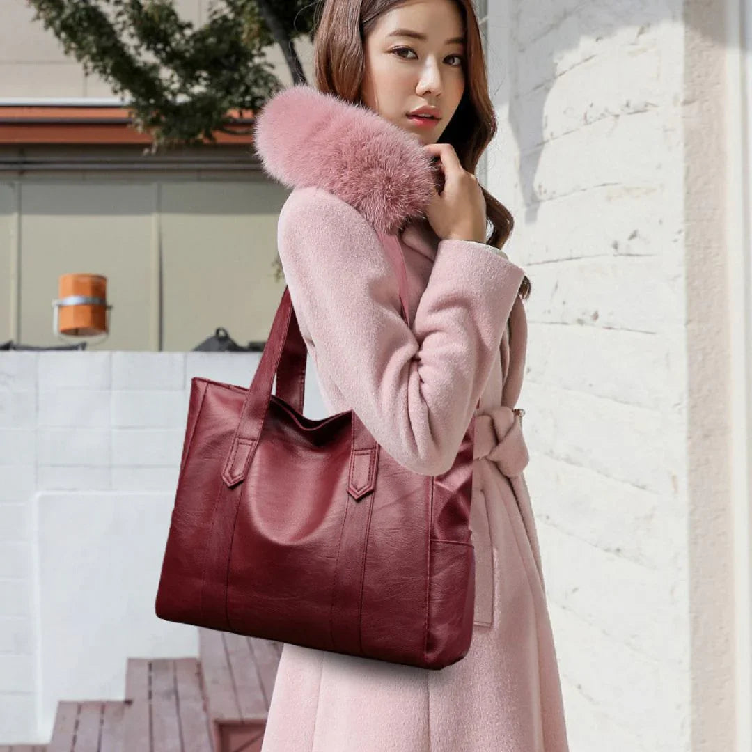 Woman in pink fur collar coat carrying a large burgundy leather tote bag outdoors
