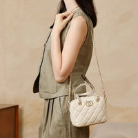 Woman in khaki vest and skirt with a small quilted cream shoulder bag