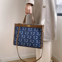 Woman holding blue and brown large tote bag with geometric F pattern, indoor setting