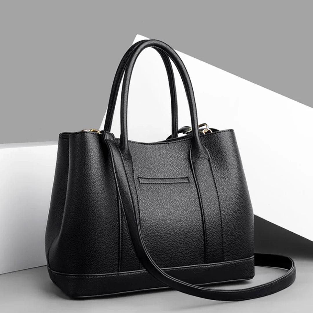 Black leather handbag with double handles and shoulder strap on a modern gray background