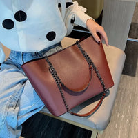 Woman in polka dot blouse with large brown leather tote bag with chain strap on lap