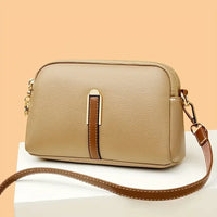 Beige leather crossbody bag with brown strap and gold hardware on a white pedestal