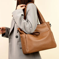 Woman in grey blazer carrying a large brown leather tote bag on shoulder