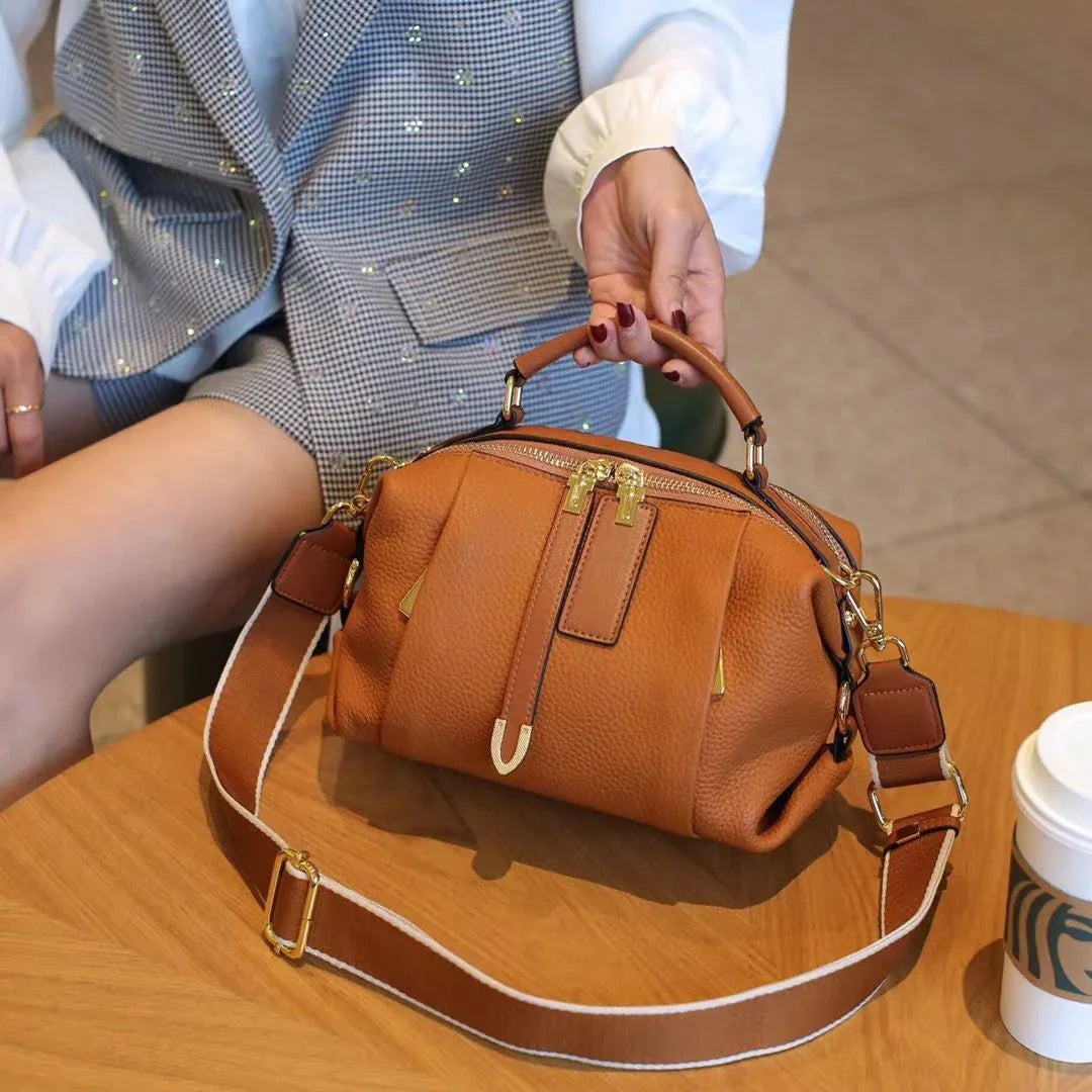 Stylish brown leather handbag with gold zippers on table, woman holding handle, coffee cup nearby