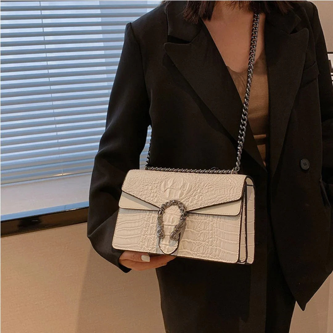 Woman in blazer holding a white crocodile-embossed shoulder bag with chain strap