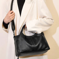 Woman in white blazer holding black leather handbag with shoulder strap